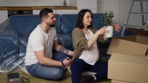 Feliz jovem casal sentado no chão na sala de estar, desempacotando coisas — Vídeo de Stock