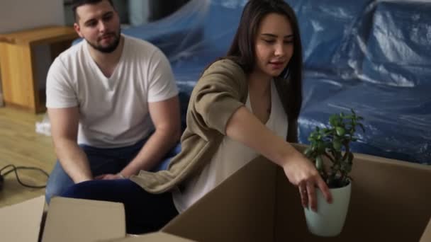 Couple joyeux assis sur le sol dans le salon, usine de déballage de la boîte — Video