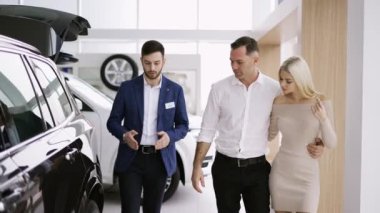 Galerideki araba satıcısını dinleyen ve lüks modelleri tartışan bir çiftin ön görüntüsü.