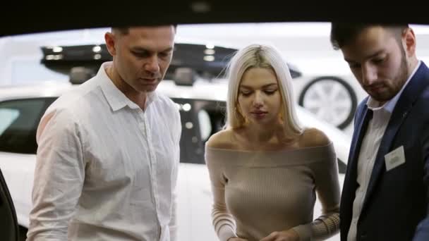 कार एजेंट ऑटोमोटिव डीलरशिप शोरूम में ग्राहकों के लिए अंदर से ट्रंक दिखा रहा है — स्टॉक वीडियो