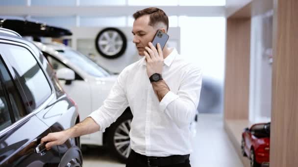 Młody człowiek korzystający z telefonu podczas wyboru nowego modelu luksusowego samochodu w salonie — Wideo stockowe
