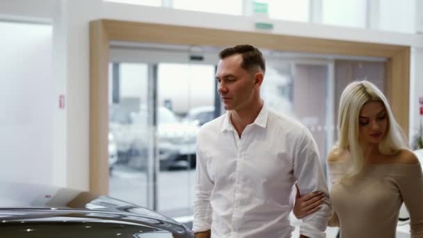 Homem com mulher loira sexy veio para escolher o carro na concessionária — Vídeo de Stock