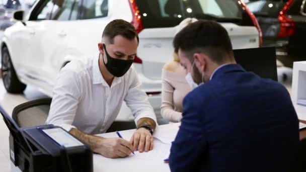 Para w maskach zakup nowego samochodu, podpisanie umowy w salonie — Wideo stockowe