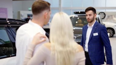 Arkadan görüntüler. Araba satıcısı ile konuşan çift seçilmiş arabayı tartışıyor.