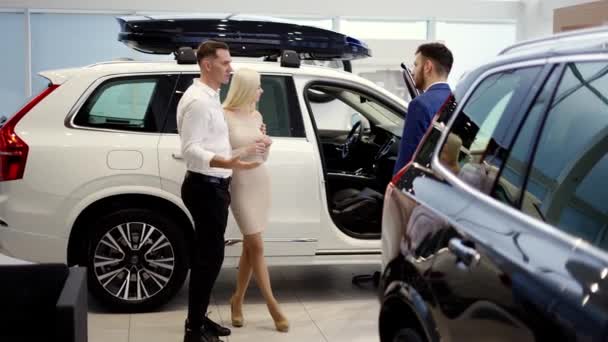 Couple talking to car dealer in dealership discussing automobiles looking at luxurious new white model — Vídeos de Stock