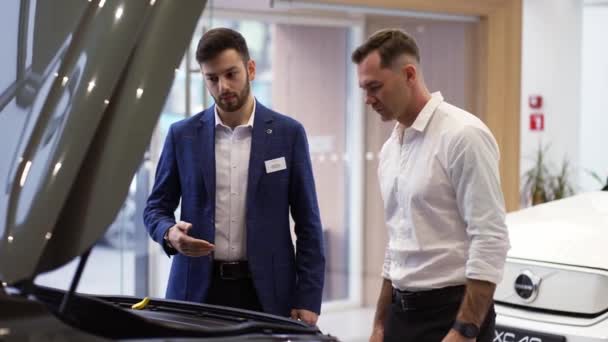 Consultant montrant le moteur de voiture sous capot ouvert à un client en salle d'exposition automobile — Video