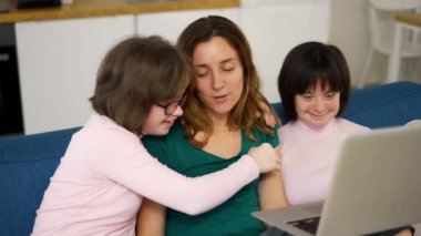 İki kızı düşük sendromlu anne kanepede oturup dizüstü bilgisayar kullanarak eğleniyor.