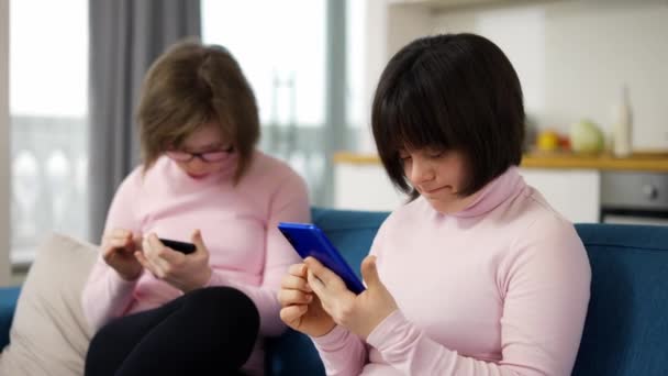 Två flickor med ner syndrom håller smartphones-titta på bilder, använda en social media app — Stockvideo