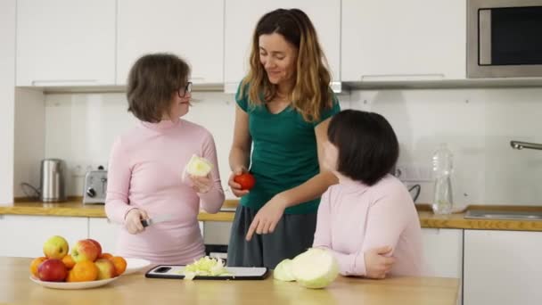 Δύο κορίτσια με σύνδρομο Down μαθαίνουν να μαγειρεύουν με τη μητέρα τους στην κουζίνα στο σπίτι. — Αρχείο Βίντεο