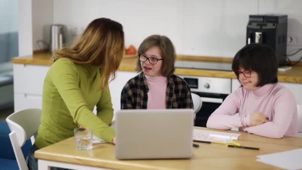 Teacher teaches young girls with down syndrome to use a laptop at the kitchen — Vídeos de Stock