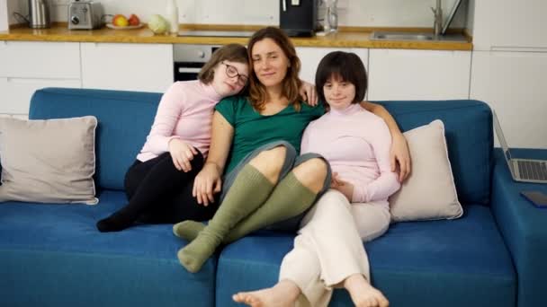 Portrét dvou dívek s Downovým syndromem sedících na gauči společně objímajících se svou matkou — Stock video