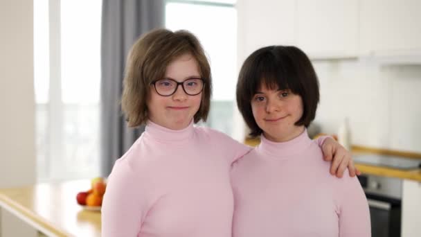 Portrét dvou roztomilých dívek s Downovým syndromem, které stojí vedle sebe a objímají se doma — Stock video