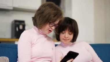Two girls with down syndrome looking at smartphones screen together on a couch