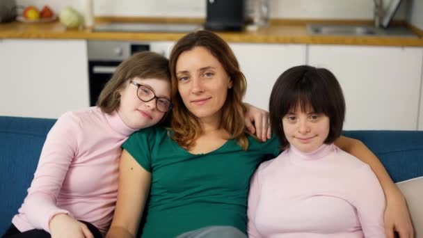 Portrait of two girls with down syndrome in sitting on a couch together embracing with their mom, close up — Vídeo de stock