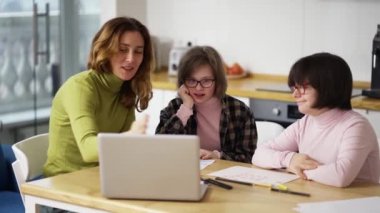 Teacher teaches young girls with down syndrome to use a laptop