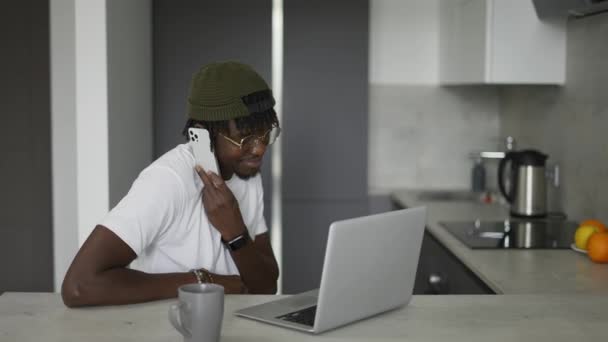 Hombre Negro Trabajando Casa Cocina Hablando Teléfono Inteligente Utilizando Ordenador — Vídeo de stock