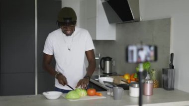 Genç Afrikalı Amerikalı adam mutfak masasında sebze salatası pişirirken taze lahana kesiyor..