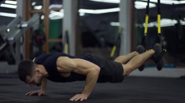 Sporcu spor salonunda TRX kayışlarıyla karın kasları egzersizi yapıyor..