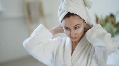 Woman at home in a bathrobe and towel and patches under the eyes.