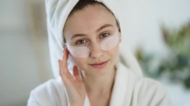 Portrait of a woman at home in a bathrobe and towel and patches under the eyes.