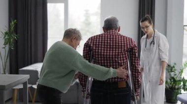 Old man making first steps with crutches at clinic.