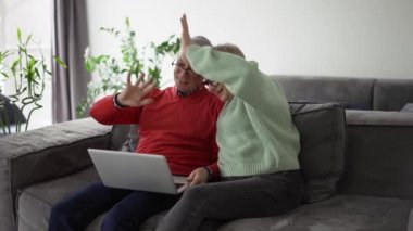 Mature couple sitting on couch and having video conference with their family on laptop.