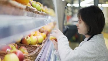 Woman with Down syndrome restocking fresh fruits in a grocery store, side view.