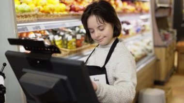 Worker with Down syndrome using a digital tablet in the fresh produce section of a grocery store.