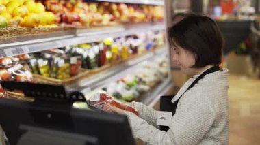Worker with Down syndrome using a digital tablet in the fresh produce section to weight the goods.