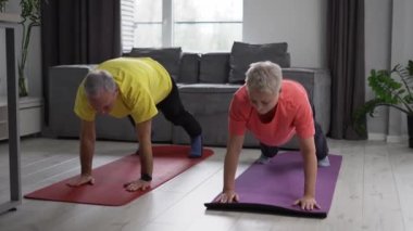 Eldery couple practicing yoga on the living room of their comfortable modern apartment.