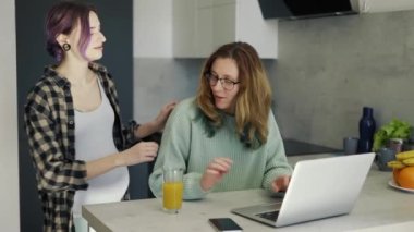 Pregnant lesbian woman embracing her partner on kitchen.