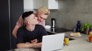 Guy working on laptop and partner holds and kiss the other.