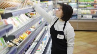 Female worker with Down syndrome restocking goods in a grocery store.