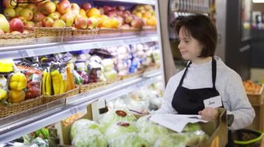 Woman with Down syndrome pushing trolley with fresh vegetables to restock the shelves.
