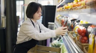 Female worker with Down syndrome restocking vegetables from the box.