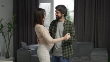 Carefree pregnant woman dancing with loving man in at home.