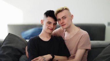 Young happy smiling homosexual male gay couple is enjoying time together is hugging on the sofa.