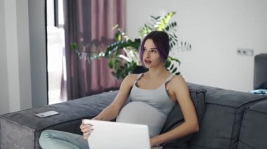 Young pregnant woman attending virtual session with doctor on laptop.