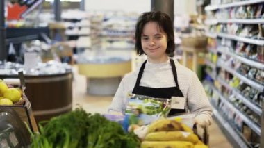 Portrait of a girl with Down syndrome pushing trolley with fresh vegetables to restock the shelves.