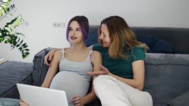 Happy gay pregnant woman using laptop computer with her wife on sofa.