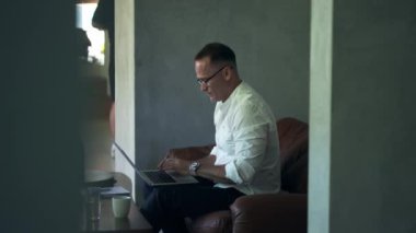 An businessman working on laptop computer. Male professional typing on laptop keyboard at caffe. Portrait of positive business man looking at laptop screen indoors.