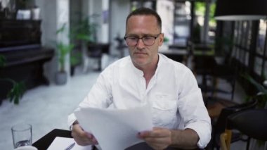Focused adult businessman working on project, writing paper notes, sitting at caffee desk. Concentrated male professional analyzing market research information.
