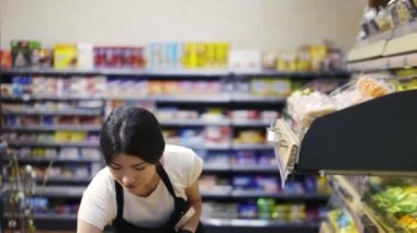 Asian girl worker puts goods on the shelf. Filling shelves with goods. Shop work.