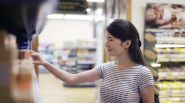 Asyalı bir kız ziyaretçi iki üründen birini seçiyor. Mutlu dükkan ziyaretçileri. Mağazadaki ürün seçimi.