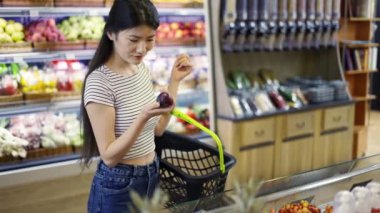 An Asian shop visitor chooses fruits and vegetables in special packages. Hold a basket in your hands.