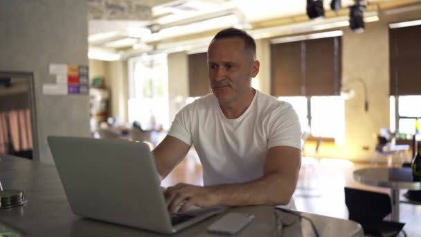 自宅のノートパソコンで働くビジネスマンの笑顔 オフィスでノートパソコンのキーボードを入力する男性の専門家 室内のノートパソコンの画面を見る正のビジネスマンの肖像画 — ストック動画