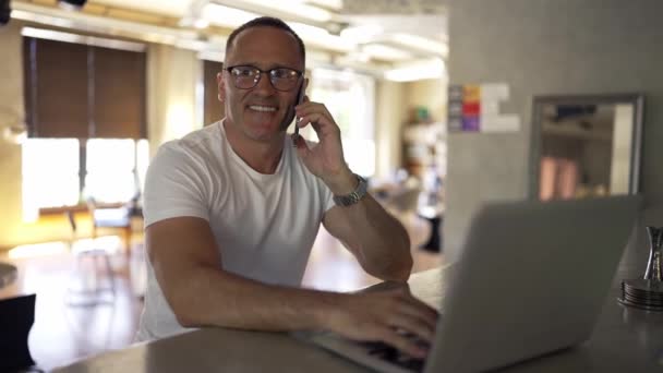 微笑的商人在总公司的笔记本电脑上工作 在家工作时 男性专业人员在笔记本电脑键盘上打字 一个积极的商人在电话中交谈的画像 — 图库视频影像