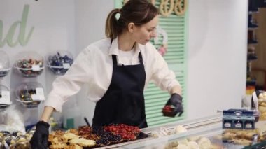 Markette siyah önlüklü bir kadın pastacı bir vitrinde pasta düzenliyor..