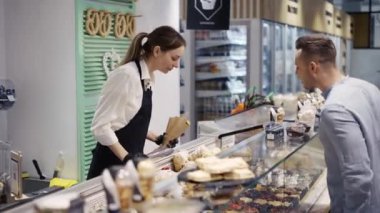 Bir ziyaretçi şekerlemeciden bir ürün seçer. Markete gidip, pasta ve hamur işi almak..