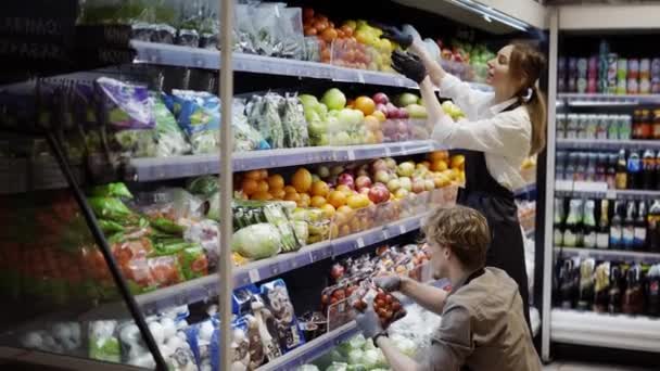 穿着黑色围裙和手套的男工在超市里为水果长袜 年轻的员工在工作 — 图库视频影像